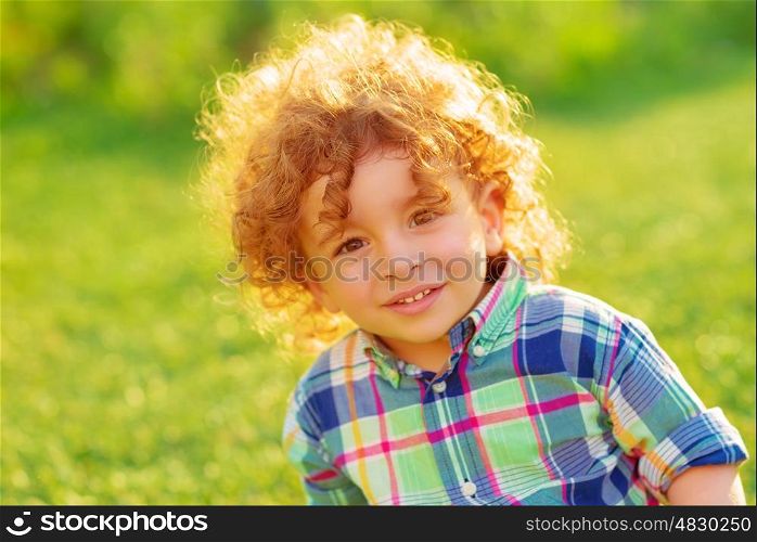 Cute cheerful boy relaxing outdoors, adorable child with beautiful curly hair spending time on green field in garden, summer holidays concept