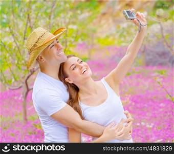 Cute cheerful couple make photo of themself outdoors on beautiful pink floral meadow in summer garden, affection and romance concept, happy weekend