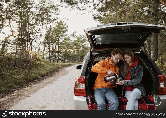 cute couple enjoying hot beverage trunk car
