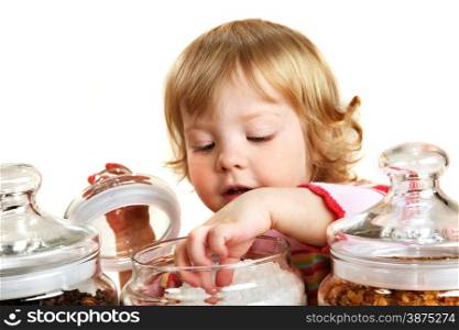 Cute curious two years girl looking into the big jars with sugar and touching it