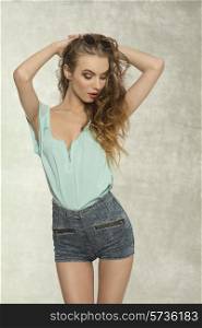 cute curly woman with perfect body, long hair and stylish make-up in fashion pose wearing denim shorts, blue shirt and vintage sunglasses on the head.