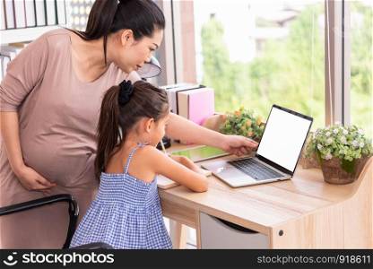 Cute daughter and her pregnant mother using white blank screen laptop at home. Parenthood and technology. Health and medical. People lifestyles and family concept. Copy space