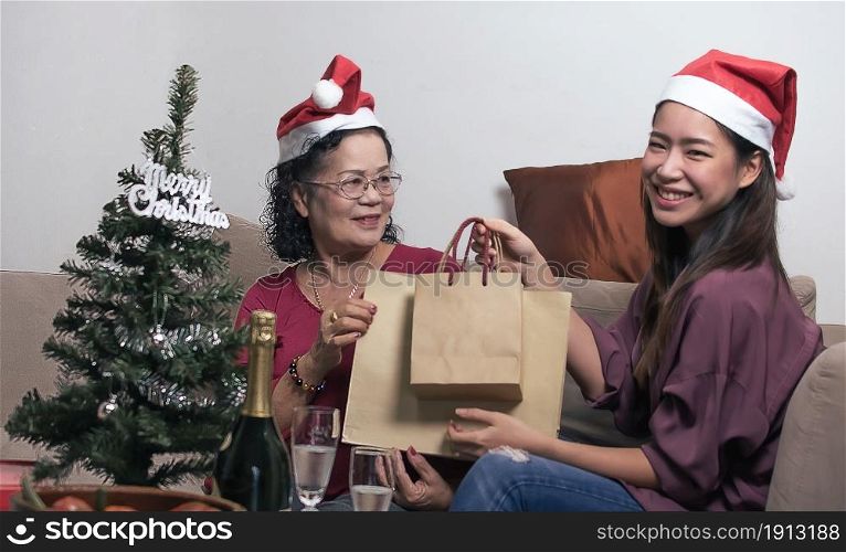 Cute daughter giving her old mother shopping bags and gifts for celebrating Christmas or New Year Party at home