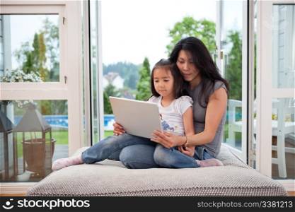 Cute daughter sitting on her mother&rsquo;s lap with laptop