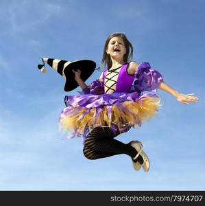 Cute Emotional Little Girl in a Costume of Witch Jumping at the Blue Sky.