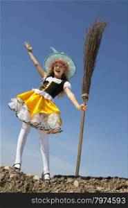 Cute Emotional Little Girl in a Costume of Witch Jumping with a Broom at the Blue Sky.