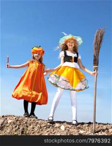 Cute Emotional Little Girls in a Costume of Witch and Pumpkin Standing with a Broom and Candy at the Blue Sky.&#xA;