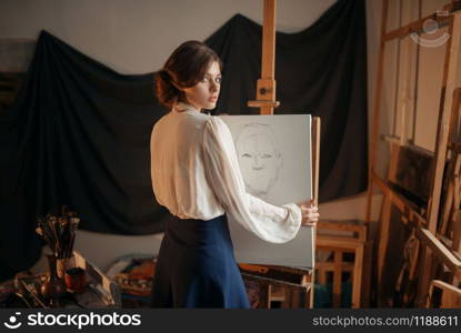 Cute female artist drawing in studio. Creative paint, pencil sketch on easel, workshop interior on background. Cute female artist drawing in studio