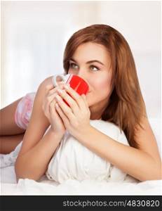 Cute female having morning coffee in the bed at home, enjoying tasty energetic beverage, happy life of young people