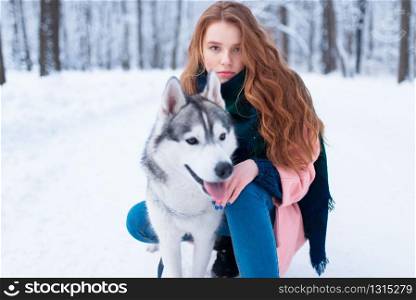 Cute female master on dog training with siberian husky, snowy forest on background. Cute girl with funs with charming pet. Female master on dog training with siberian husky