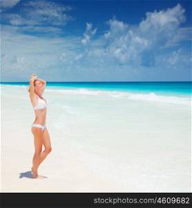 Cute female suntanning on seashore, standing with raised up hands on the beach and enjoying warm sunlight, luxury tropical resort, summer vacation