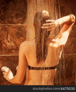 Cute female taking shower outside, rear view, enjoying warm falling water drops and bright sun light, healthy lifestyle, luxury spa resort, freshness and pleasure concept