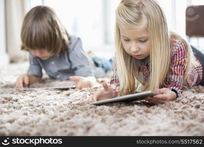 Cute girl and brother using digital tablets on rug in living room