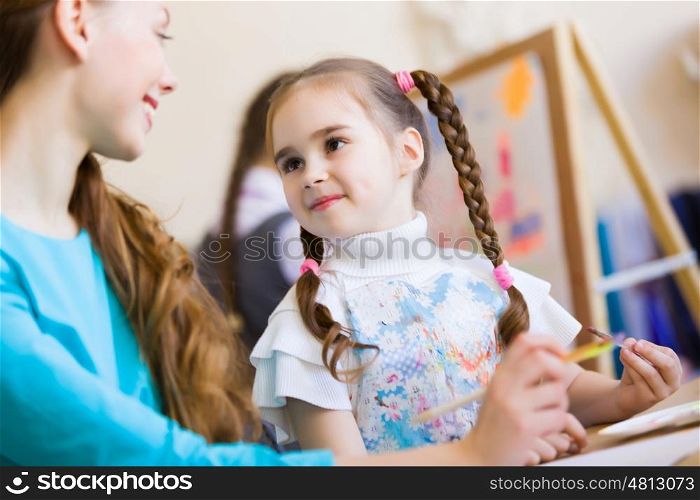 Cute girl and teacher. Little girl painting with teacher at kindergarten