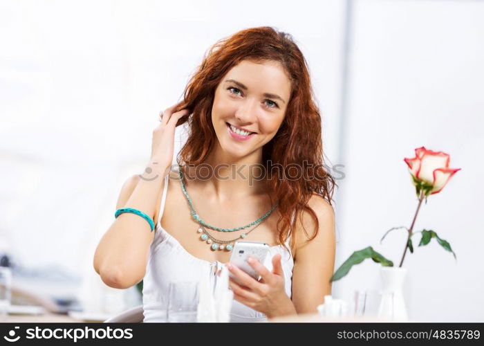 Cute girl at cafe. Portrait of young pretty woman sitting at cafe and using mobile phone