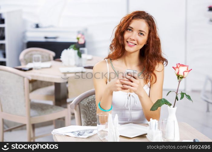 Cute girl at cafe. Portrait of young pretty woman sitting at cafe and using mobile phone