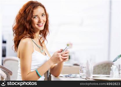Cute girl at cafe. Portrait of young pretty woman sitting at cafe and using mobile phone