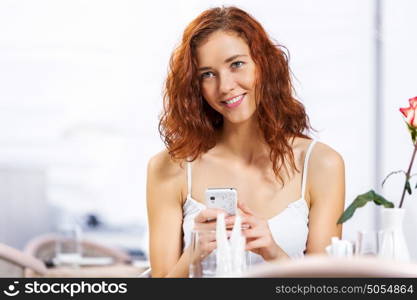 Cute girl at cafe. Portrait of young pretty woman sitting at cafe and using mobile phone