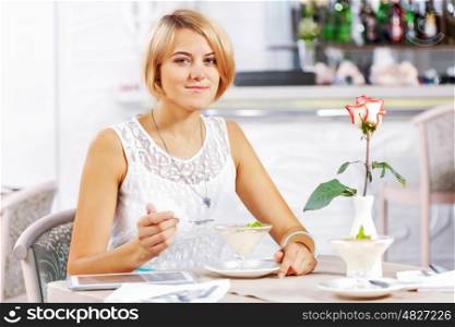 Cute girl at cafe. Portrait of young pretty woman sitting at cafe and eating dessert