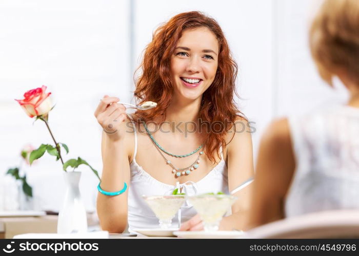 Cute girl at cafe. Two young pretty women sitting at cafe and eating dessert