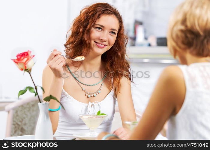 Cute girl at cafe. Two young pretty women sitting at cafe and eating dessert