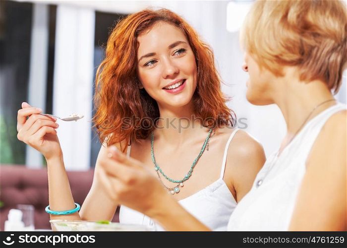 Cute girl at cafe. Two young pretty women sitting at cafe and eating dessert