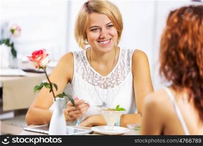 Cute girl at cafe. Two young pretty women sitting at cafe and eating dessert