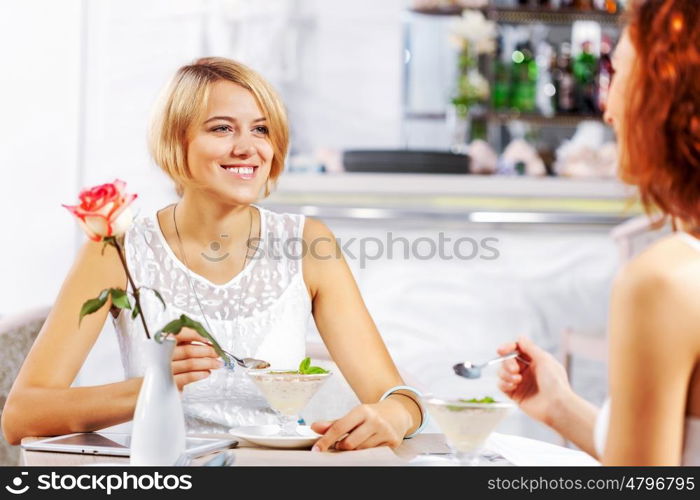 Cute girl at cafe. Two young pretty women sitting at cafe and eating dessert