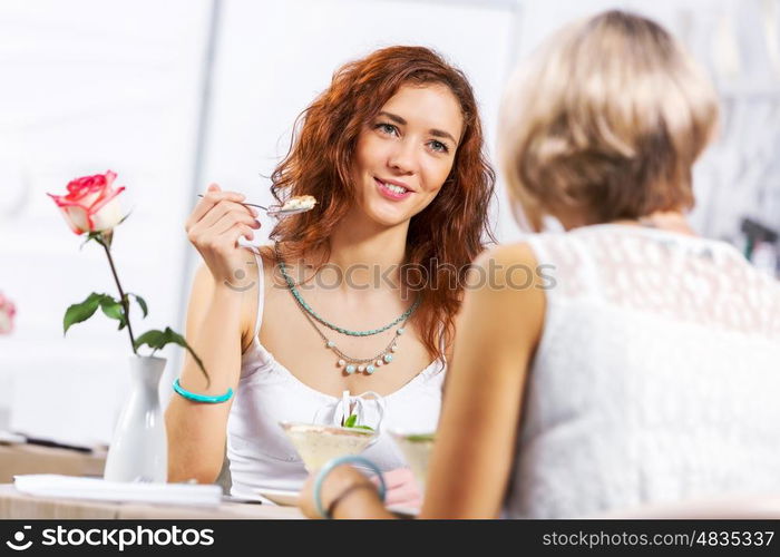 Cute girl at cafe. Two young pretty women sitting at cafe and eating dessert