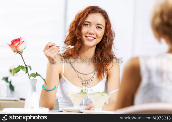 Cute girl at cafe. Two young pretty women sitting at cafe and eating dessert