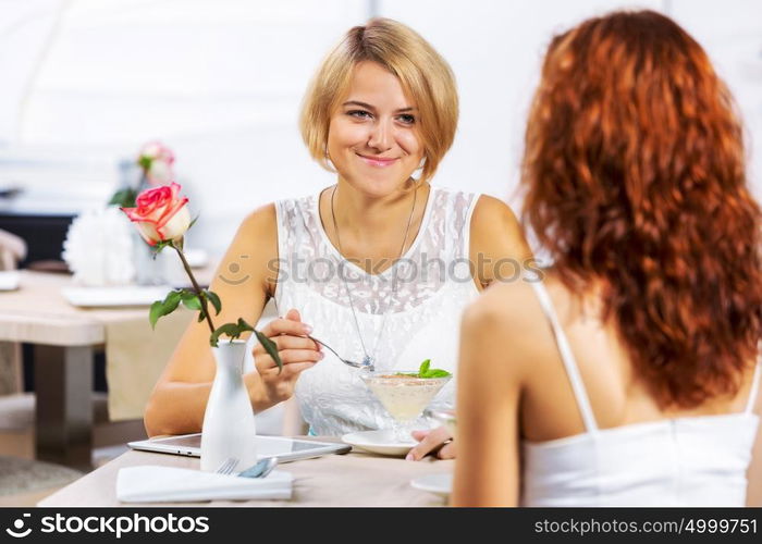 Cute girl at cafe. Two young pretty women sitting at cafe and eating dessert