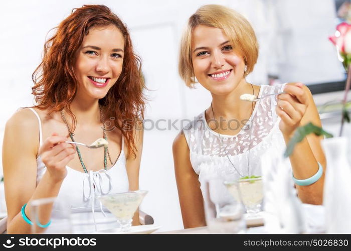 Cute girl at cafe. Two young pretty women sitting at cafe and eating dessert