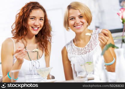 Cute girl at cafe. Two young pretty women sitting at cafe and eating dessert