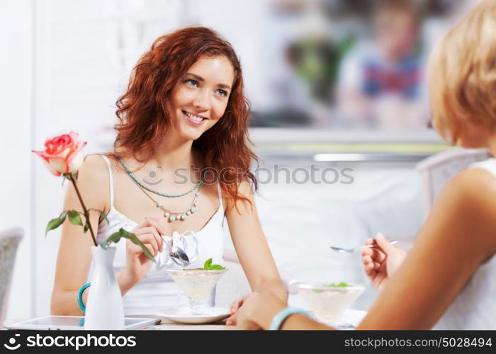 Cute girl at cafe. Two young pretty women sitting at cafe and eating dessert