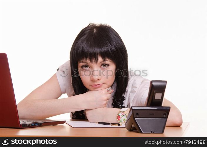 Cute girl at the table in the call center rested her head on his folded arms and a tired look in the picture. Tortured call-center employee at the desk