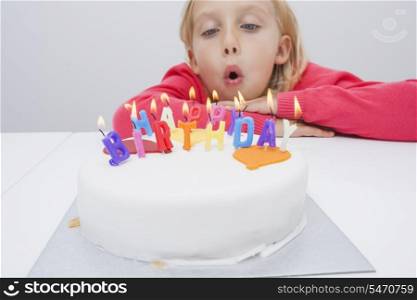 Cute girl blowing birthday candles at table in house