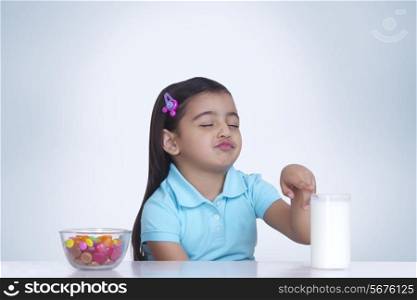 Cute girl choosing between milk and bowl of sweet food against blue background