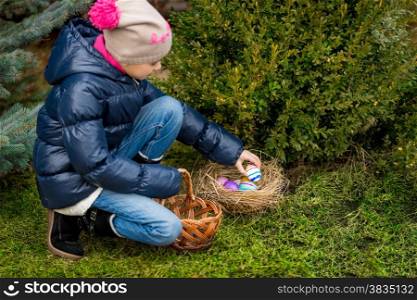 Cute girl collecting colorful Easter eggs in the basket at backyard