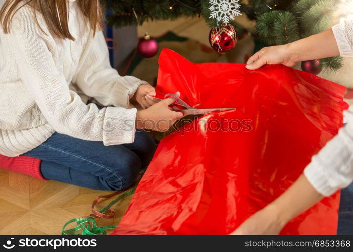 Cute girl cutting red paper for wrapping Christmas presents