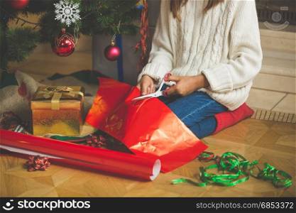 Cute girl cutting wrapping paper under Christmas tree at living room