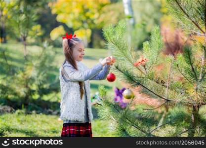 Cute girl decorating the Christmas tree outdoors in the yard before the holidays. Merry Christmas and happy holidays.. Cute girl decorating the Christmas tree outdoors in the yard before the holidays.