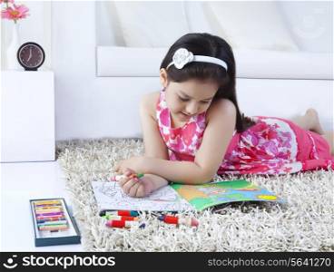 Cute girl drawing in book while lying on rug at home