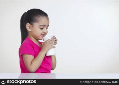 Cute girl drinking glass of milk against white background