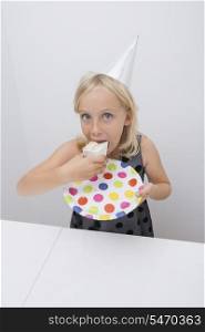 Cute girl eating birthday cake slice at table in house