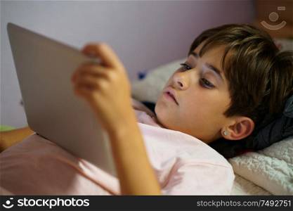 Cute girl, eight years old, using a tablet computer in her bedroom. Girl with short hair.. Cute girl using a tablet computer in her bedroom