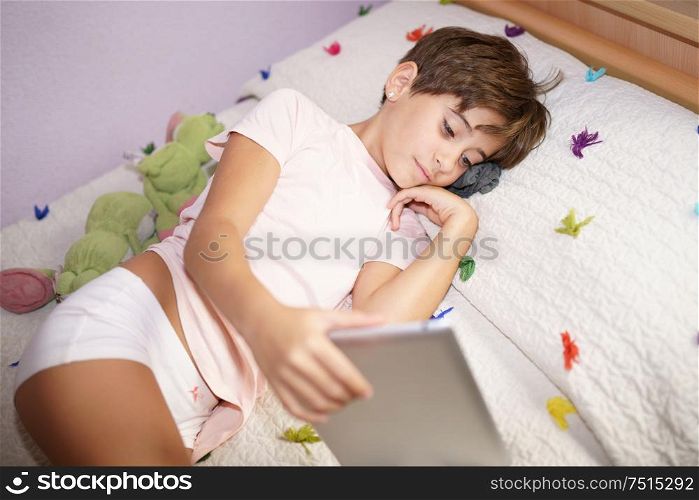 Cute girl, eight years old, using a tablet computer in her bedroom. Girl with short hair.. Cute girl using a tablet computer in her bedroom