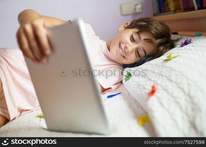 Cute girl, eight years old, using a tablet computer in her bedroom. Girl with short hair.. Cute girl using a tablet computer in her bedroom