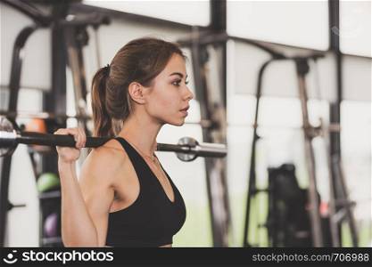 Cute girl has a hard athletic workout in the gym, doing exercises with barbells.