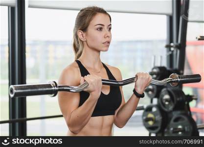 Cute girl has a hard athletic workout in the gym, doing exercises with barbells.