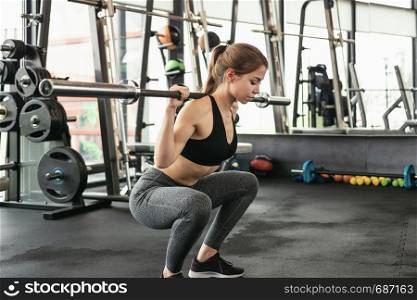 Cute girl has a hard athletic workout in the gym, doing squats with barbells.